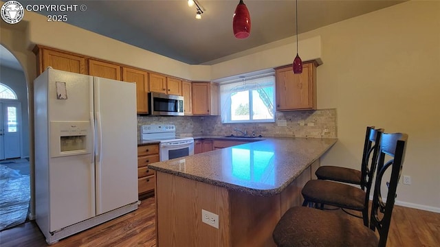 1002 Cedarcrest Dr, Pueblo, CO 81005 - kitchen featuring white appliances, a peninsula, decorative backsplash, and dark wood-style floors