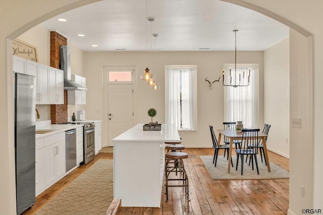 kitchen featuring stainless steel appliances, hanging light fixtures, a kitchen island, and wall chimney range hood