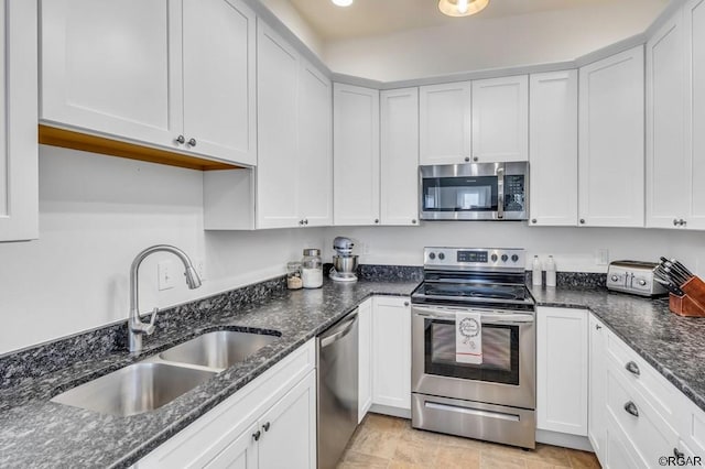 kitchen with white cabinetry, stainless steel appliances, sink, and dark stone countertops