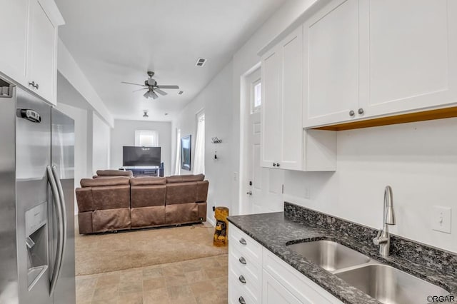 kitchen with sink, stainless steel fridge with ice dispenser, ceiling fan, dark stone counters, and white cabinets