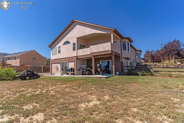 rear view of house with fence, stucco siding, a balcony, a yard, and a patio