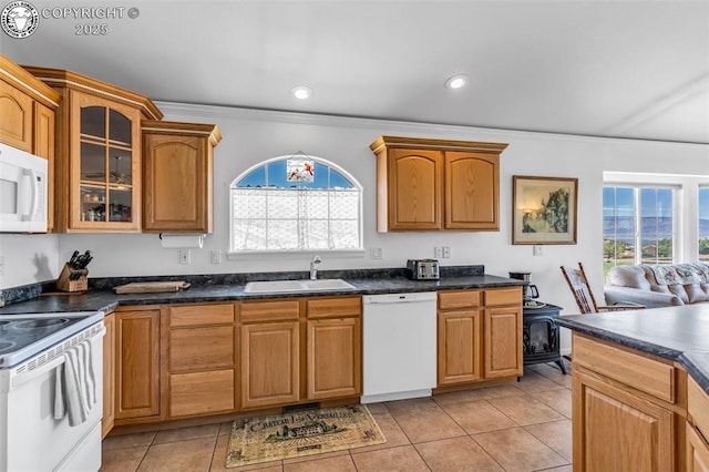 kitchen with a sink, dark countertops, white appliances, light tile patterned floors, and glass insert cabinets