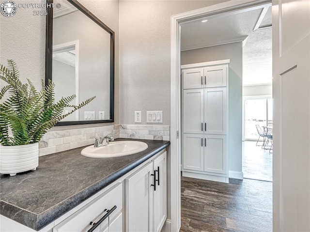 bathroom featuring vanity, wood-type flooring, ornamental molding, and tasteful backsplash