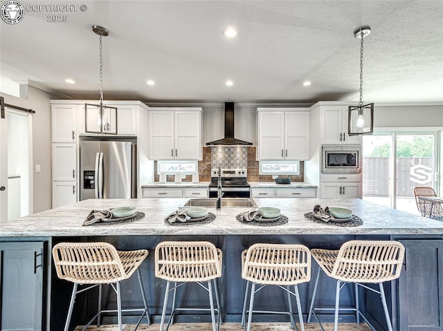 kitchen featuring wall chimney range hood, stainless steel appliances, white cabinets, a barn door, and a large island with sink