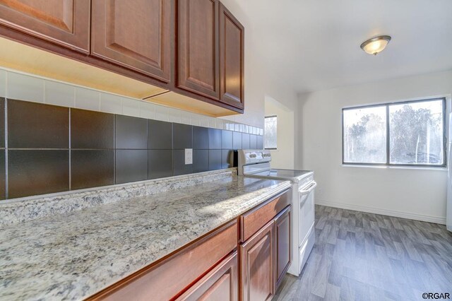 kitchen featuring backsplash, light stone countertops, light hardwood / wood-style flooring, and white range with electric stovetop