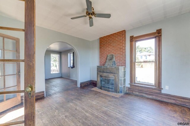 unfurnished living room with ceiling fan, a large fireplace, dark hardwood / wood-style flooring, and a wealth of natural light