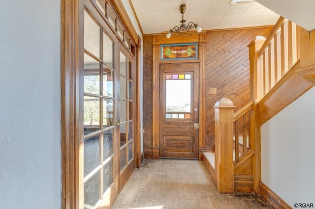 doorway to outside with an inviting chandelier, wooden walls, light parquet flooring, and plenty of natural light