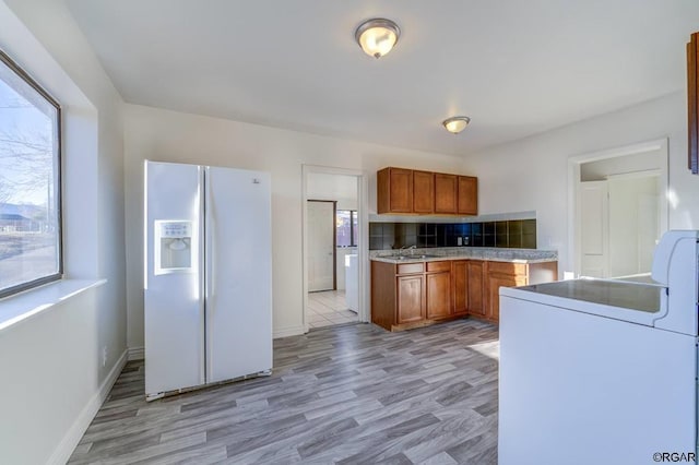 kitchen featuring sink, tasteful backsplash, white fridge with ice dispenser, washer / clothes dryer, and light wood-type flooring