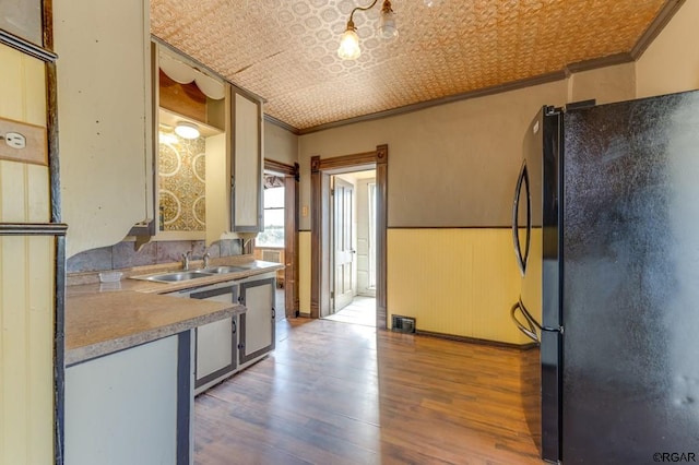 kitchen featuring sink, ornamental molding, hardwood / wood-style floors, and black fridge