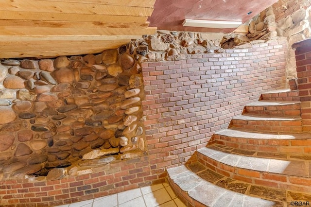 stairway with tile patterned flooring, beamed ceiling, and brick wall