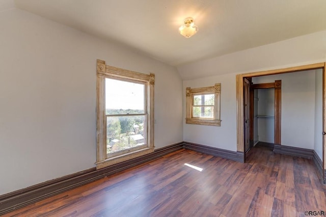 unfurnished bedroom with dark hardwood / wood-style flooring, multiple windows, vaulted ceiling, and a closet