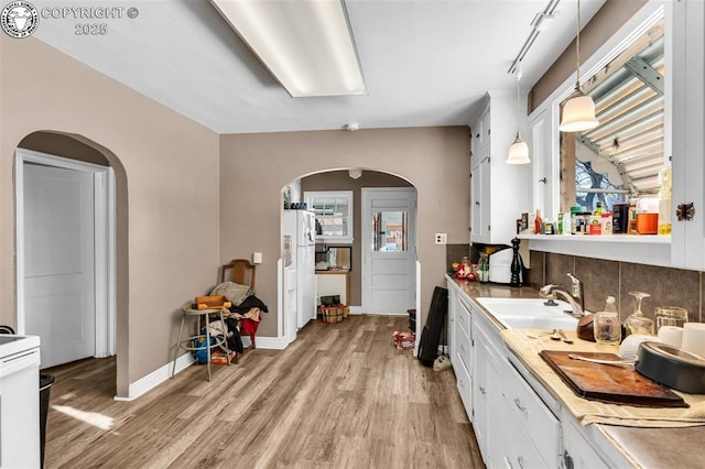 kitchen featuring sink, white appliances, light hardwood / wood-style flooring, white cabinets, and decorative light fixtures