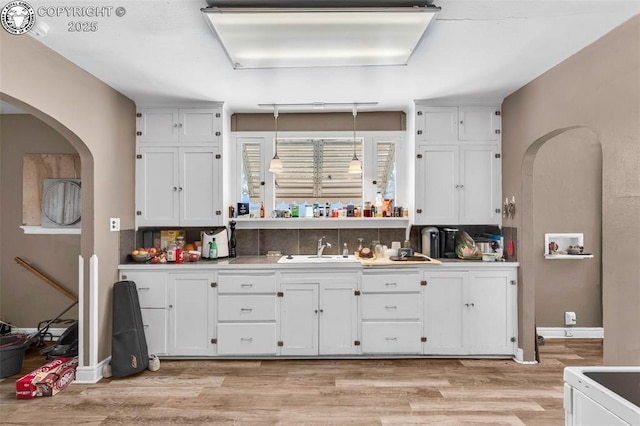 kitchen with white cabinetry, sink, light hardwood / wood-style floors, and decorative backsplash