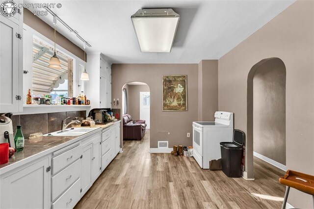 interior space with white electric range oven, sink, white cabinetry, pendant lighting, and light hardwood / wood-style floors