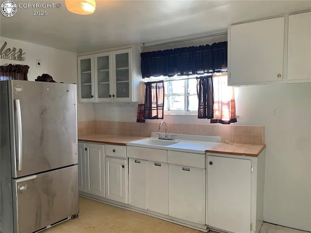 kitchen with glass insert cabinets, freestanding refrigerator, white cabinets, and a sink