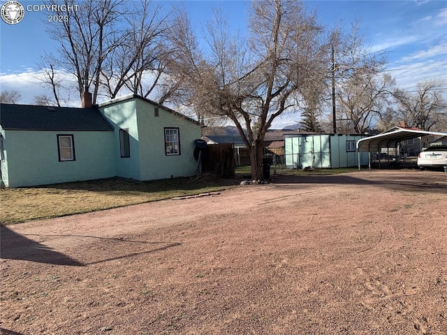 view of front of property featuring dirt driveway, a chimney, a detached carport, and stucco siding