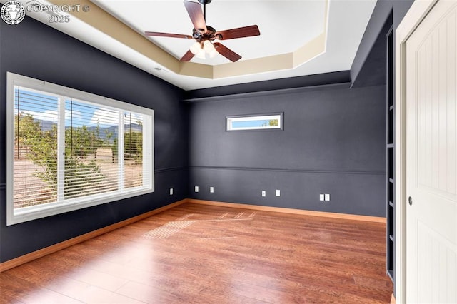 empty room with ceiling fan, a raised ceiling, and hardwood / wood-style floors