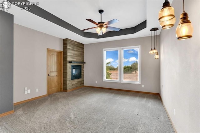 unfurnished living room featuring ceiling fan, carpet, a fireplace, and a tray ceiling