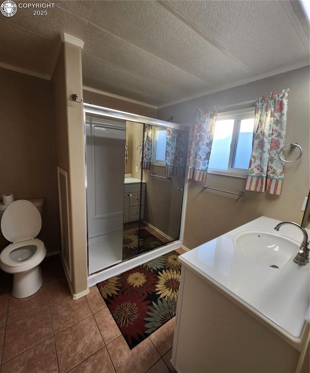 bathroom with walk in shower, toilet, a textured ceiling, vanity, and tile patterned flooring