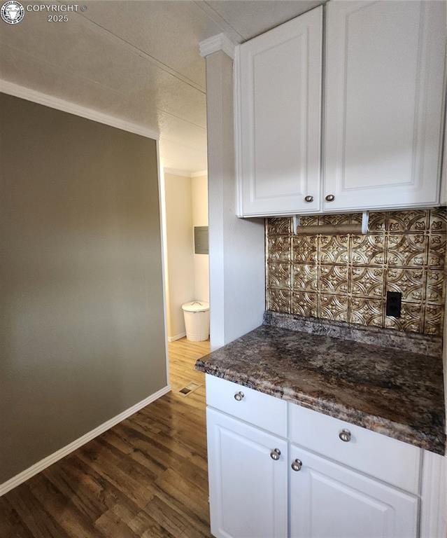 kitchen with ornamental molding, dark wood-type flooring, dark stone countertops, and white cabinets