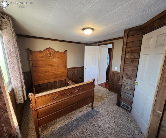 carpeted bedroom featuring crown molding, a textured ceiling, and wood walls