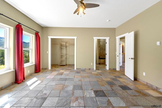 unfurnished bedroom featuring multiple windows, a spacious closet, ceiling fan, and a closet