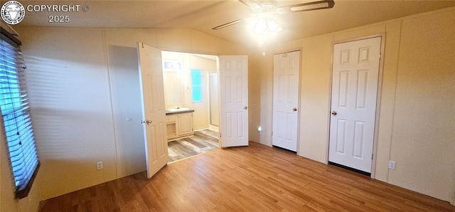 unfurnished bedroom featuring ceiling fan, lofted ceiling, ensuite bathroom, and light wood-type flooring