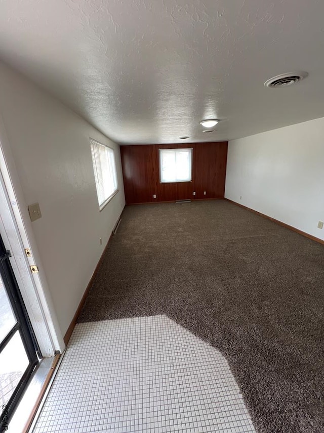 empty room with carpet floors, a textured ceiling, and wood walls