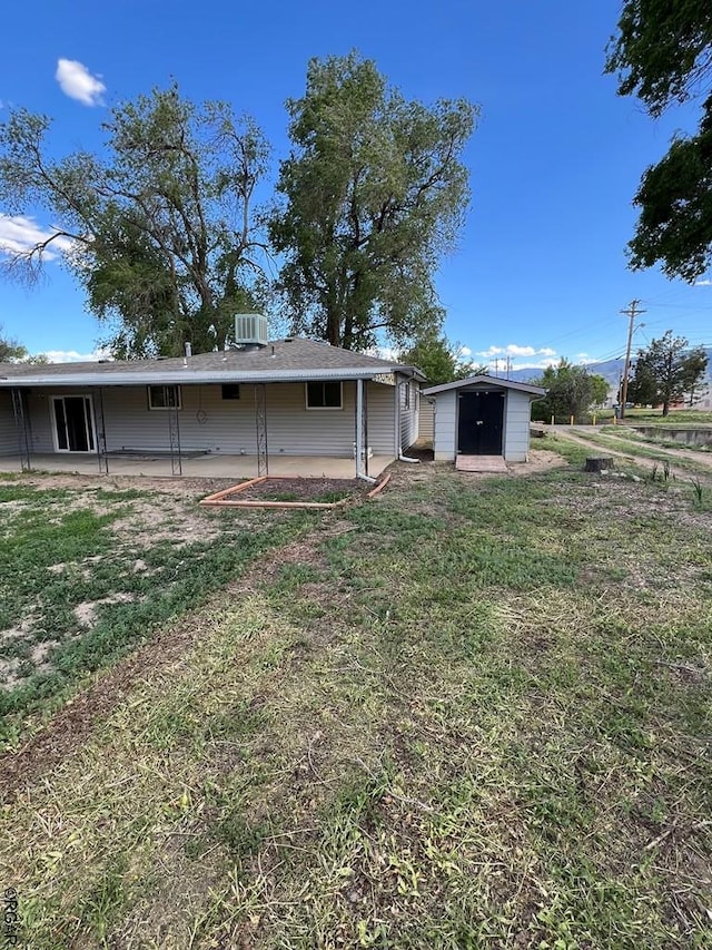 back of property with a storage unit, a yard, and central air condition unit