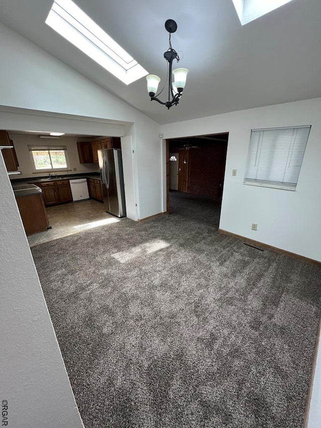 unfurnished living room with an inviting chandelier, dark carpet, and vaulted ceiling with skylight