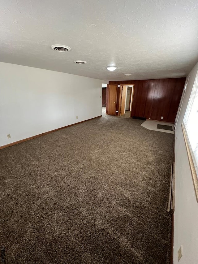 carpeted spare room with a textured ceiling and wooden walls