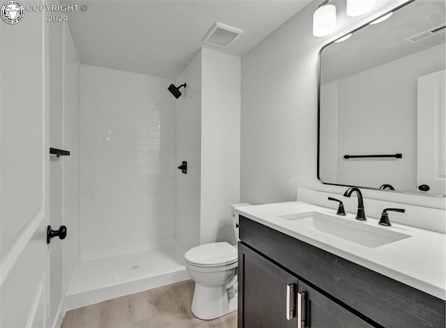 bathroom featuring hardwood / wood-style flooring, vanity, tiled shower, and toilet