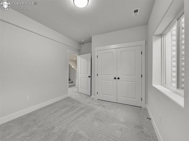 unfurnished bedroom featuring light colored carpet, a textured ceiling, and a closet