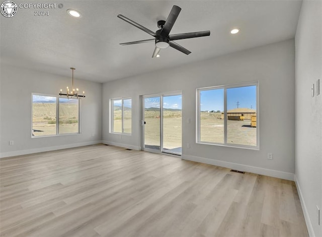 spare room with ceiling fan with notable chandelier and light hardwood / wood-style floors