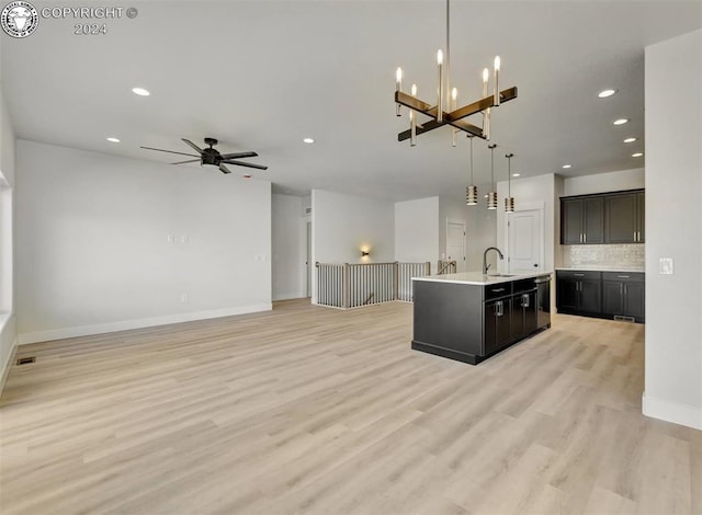 kitchen with tasteful backsplash, a kitchen island with sink, pendant lighting, and light wood-type flooring