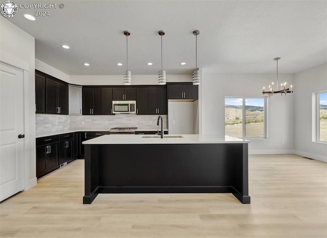 kitchen featuring sink, appliances with stainless steel finishes, backsplash, a center island with sink, and decorative light fixtures