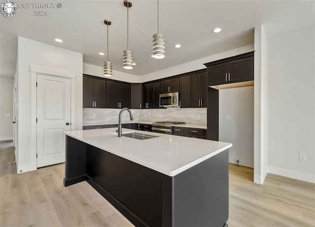 kitchen featuring sink, hanging light fixtures, stainless steel appliances, light hardwood / wood-style floors, and an island with sink