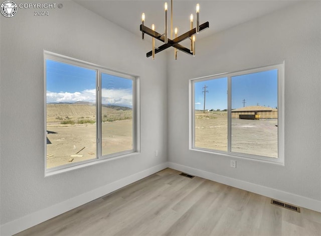 empty room featuring plenty of natural light, light wood-type flooring, and a chandelier