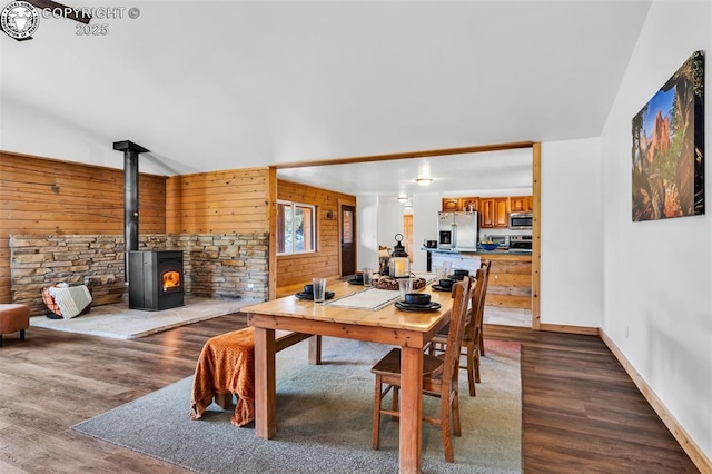 dining space with hardwood / wood-style flooring, wooden walls, and a wood stove