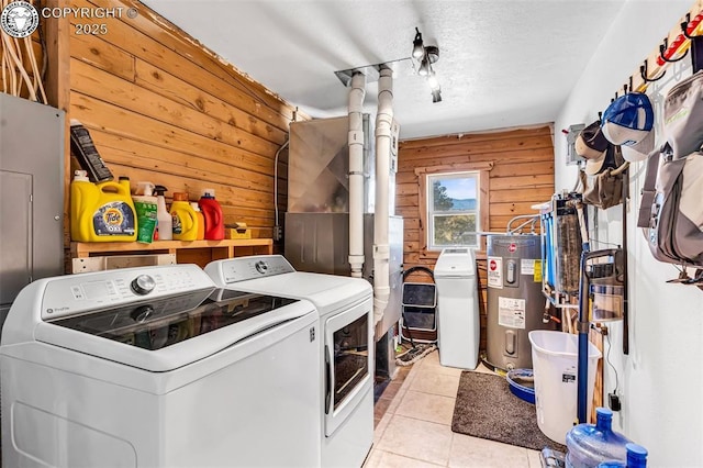 laundry room featuring electric water heater, light tile patterned floors, washer and clothes dryer, and wood walls