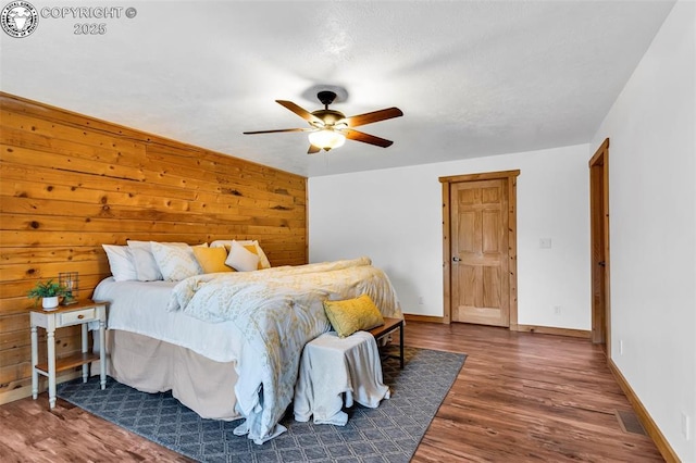 bedroom with ceiling fan, dark hardwood / wood-style flooring, and wood walls