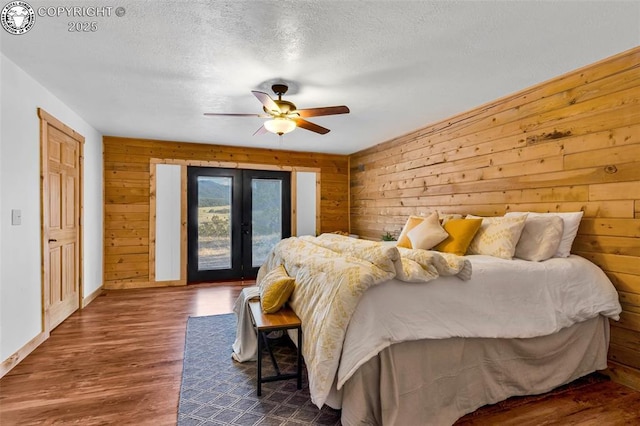 bedroom with ceiling fan, access to exterior, wooden walls, a textured ceiling, and french doors