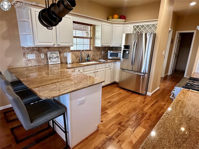 kitchen featuring stainless steel appliances, white cabinetry, a sink, a peninsula, and a kitchen breakfast bar