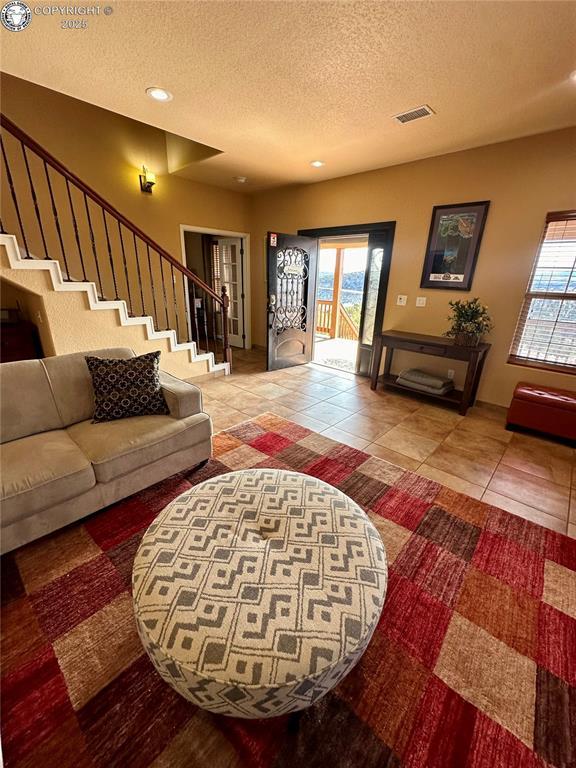 living room with a textured ceiling, stairway, tile patterned flooring, and visible vents