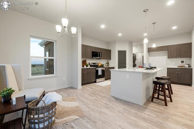 kitchen with appliances with stainless steel finishes, a kitchen island with sink, hanging light fixtures, and light wood-type flooring