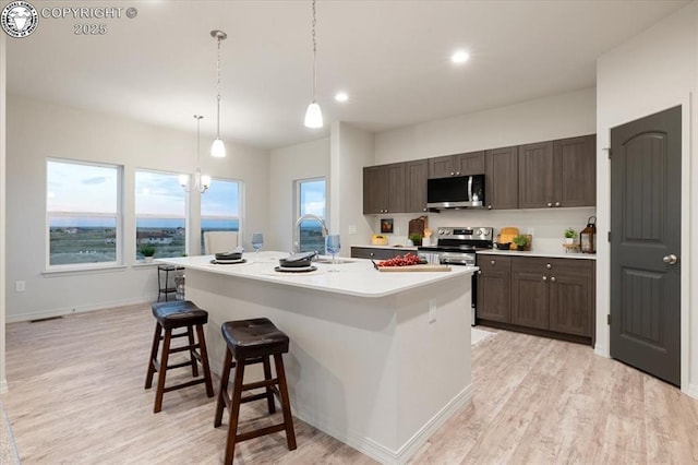 kitchen with sink, dark brown cabinets, a center island with sink, appliances with stainless steel finishes, and pendant lighting