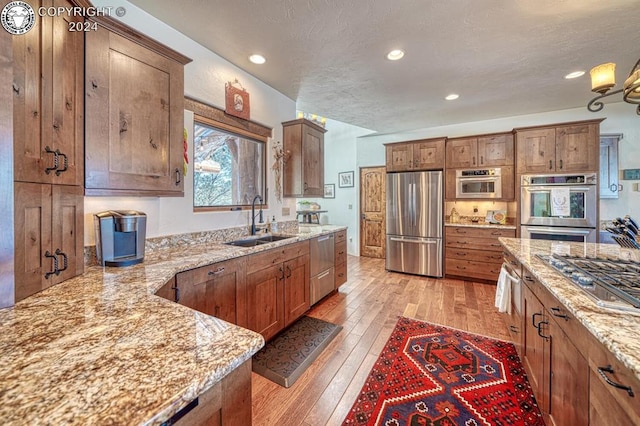 kitchen featuring appliances with stainless steel finishes, sink, light wood-type flooring, light stone counters, and a textured ceiling