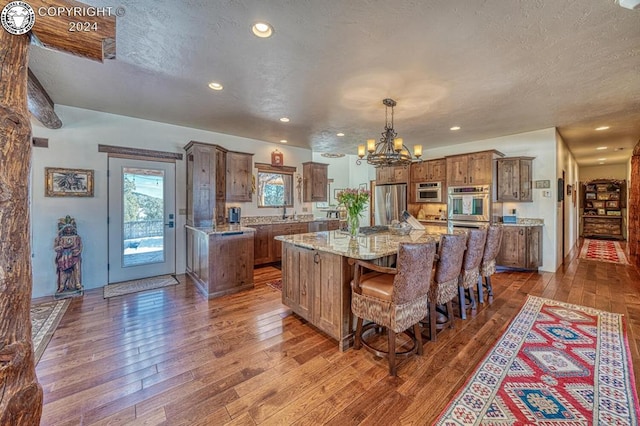 kitchen featuring dark wood-type flooring, appliances with stainless steel finishes, a spacious island, light stone countertops, and decorative light fixtures