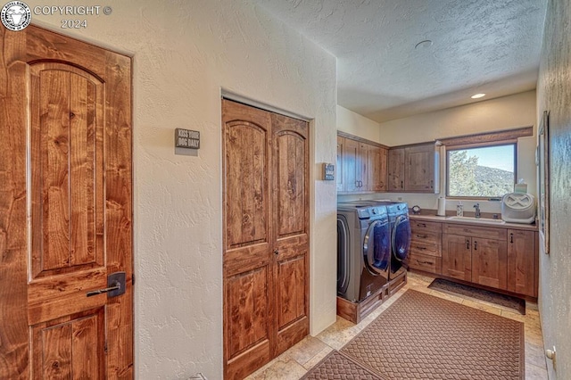 clothes washing area with light tile patterned flooring, sink, cabinets, washer and clothes dryer, and a textured ceiling