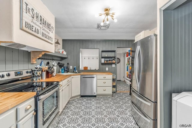 kitchen with stainless steel appliances, butcher block counters, sink, and white cabinets